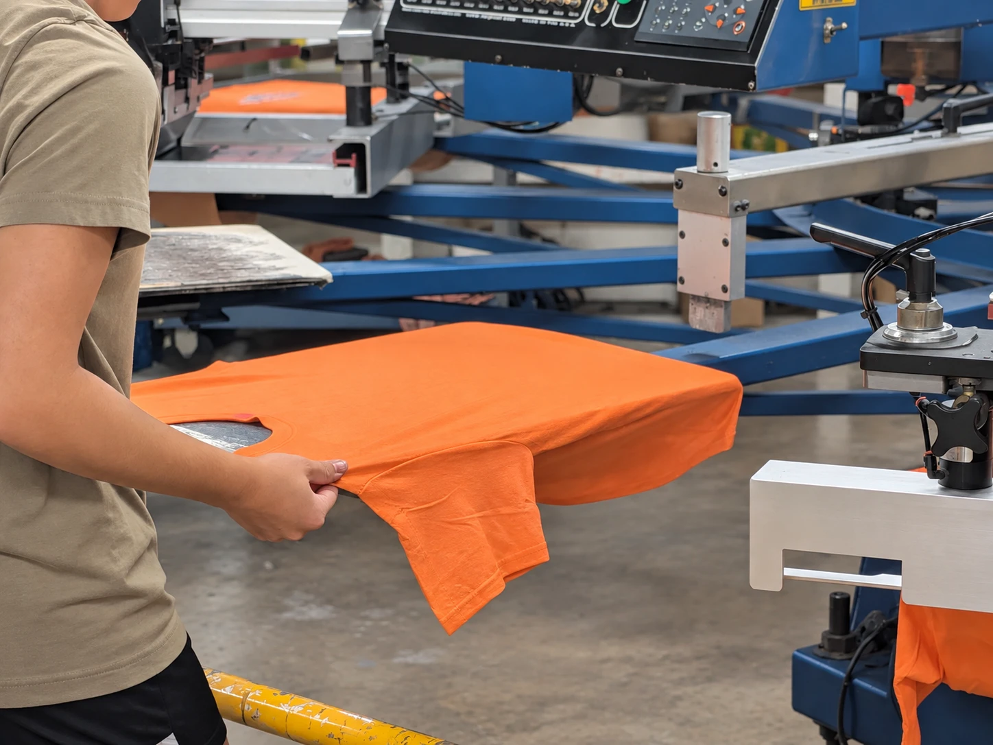 Edited photo of a Del Print employee loading an orange shirt onto the press